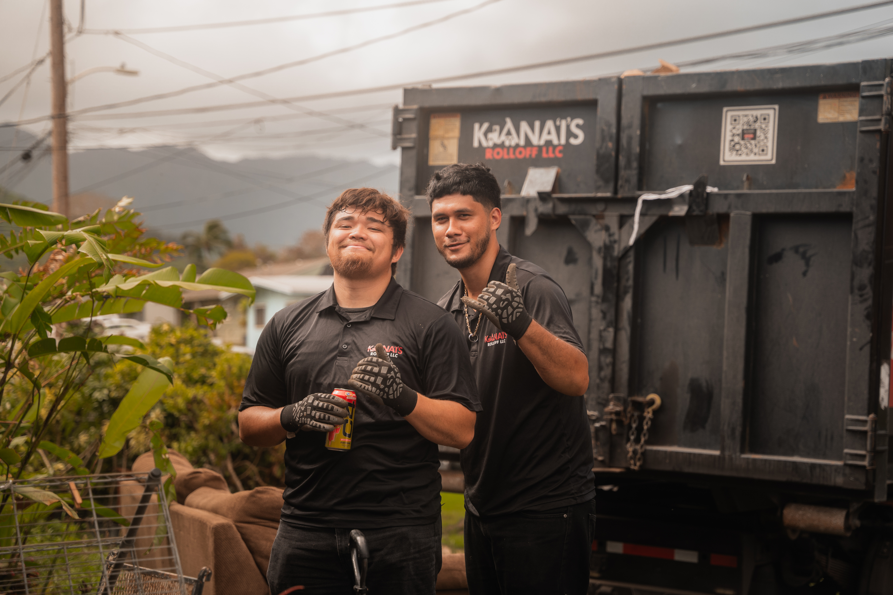 Two Kana'i's Junk Removal techs holding up shaka signs while taking bulky items out of a home in Oahu.