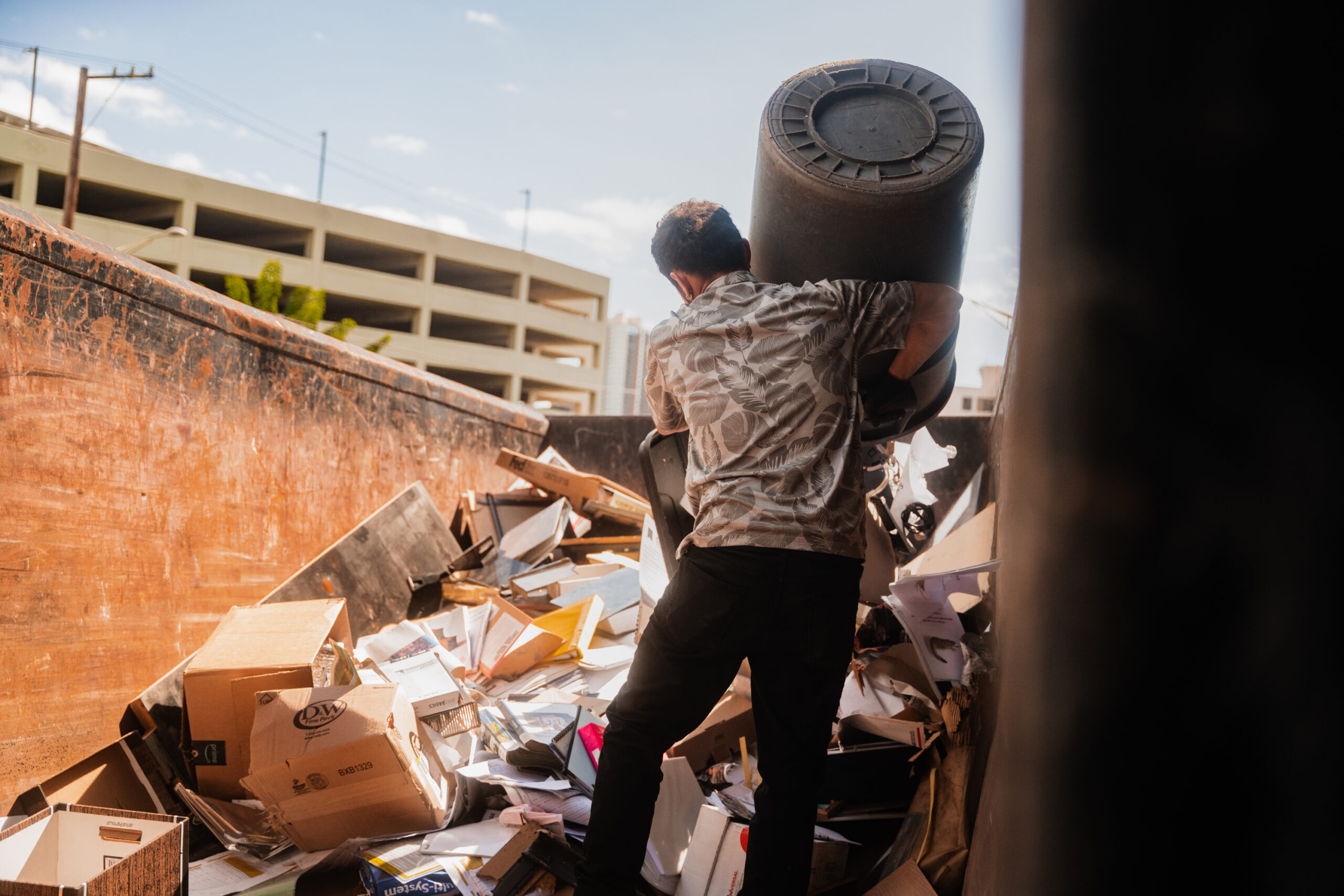 A Kana'i's Junk Removal employee emptying a garbage can full of junk into a dumpster in Aiea, Oahu.