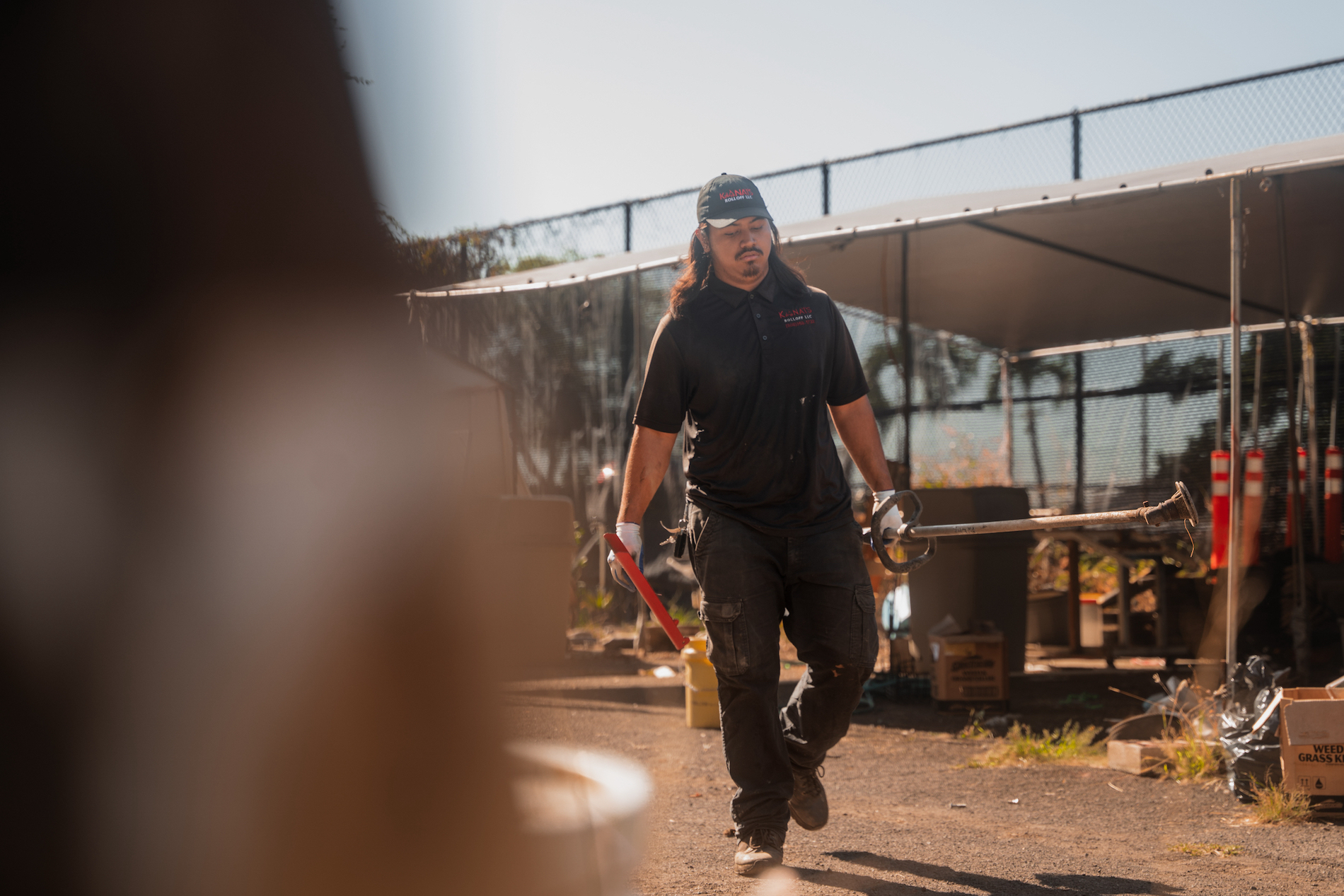 A junk removal specialist walking outside at a jobsite in Kaneohe, Oahu carrying a weed whacker.