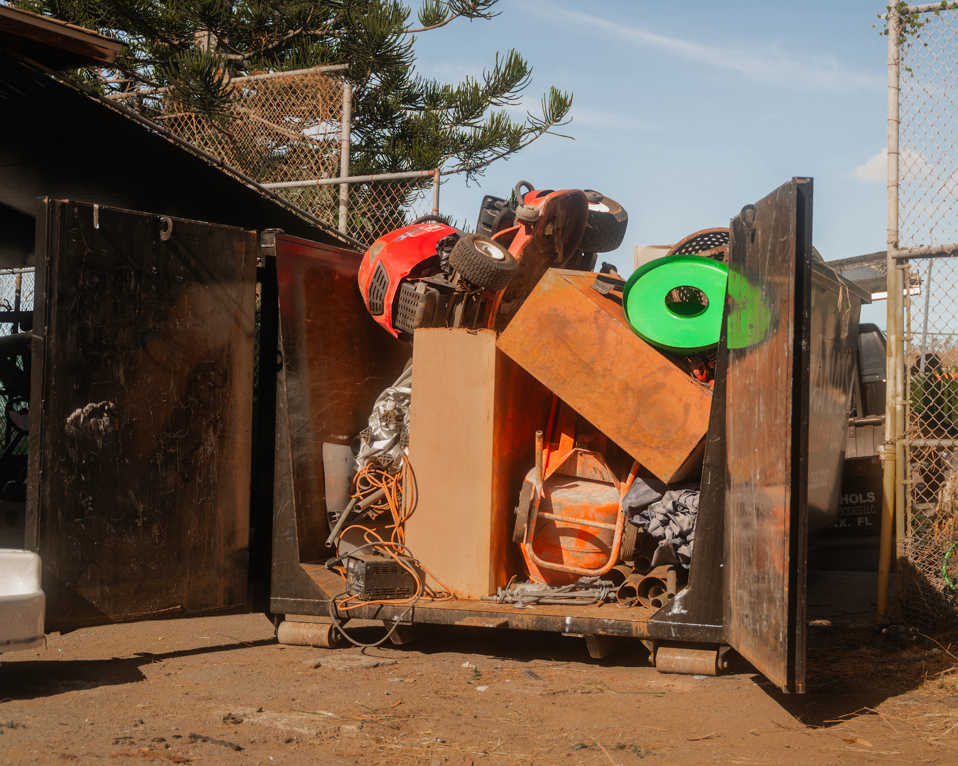 A Kana'i's Junk Removal rental dumpster being used by a local customer which is filled to the top with a lawnmower and other large equipment.